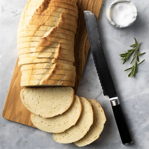 Sliced bread with a knife and rosemary on a cutting board with a marble background.